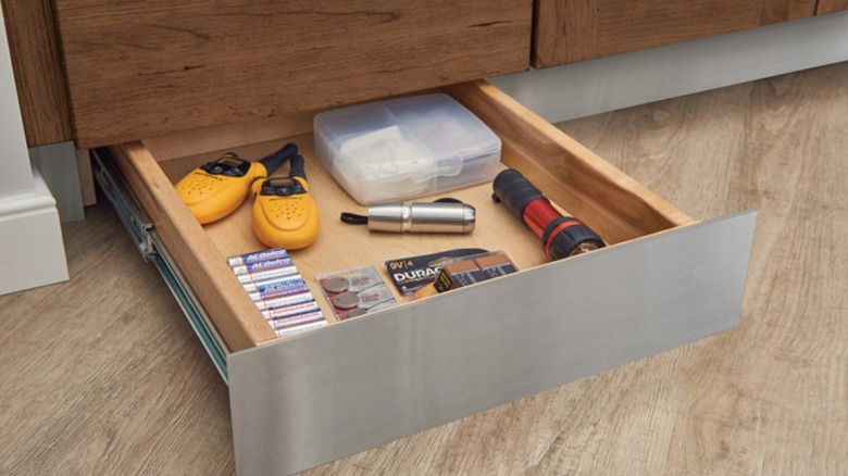 Toe kick drawer with junk drawer items like batteries and flashlights