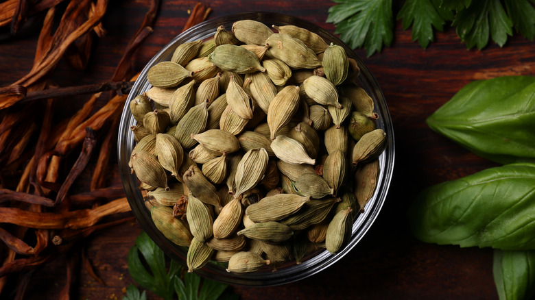 Cardamom pods in glass bowl on wooden surface