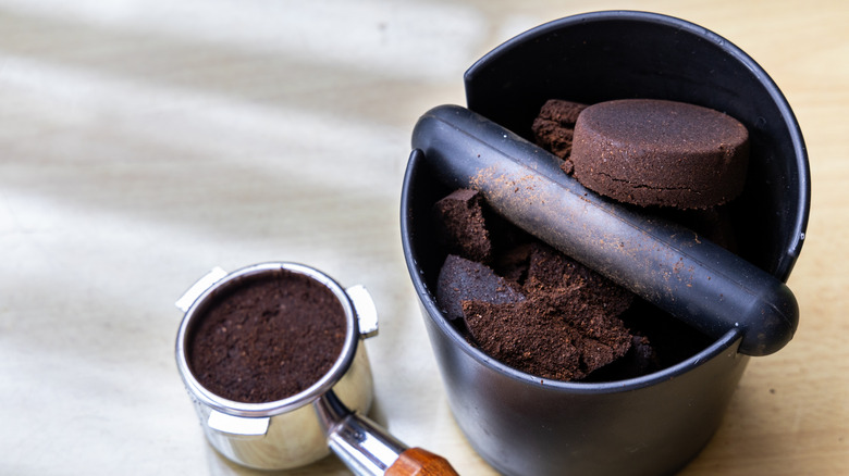 A bucket of used espresso pucks and a full espresso portafilter