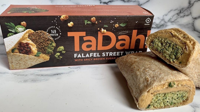 A TaDah falafel street wrap with spicy brown sugar harissa sliced in half and displayed next to the packaging