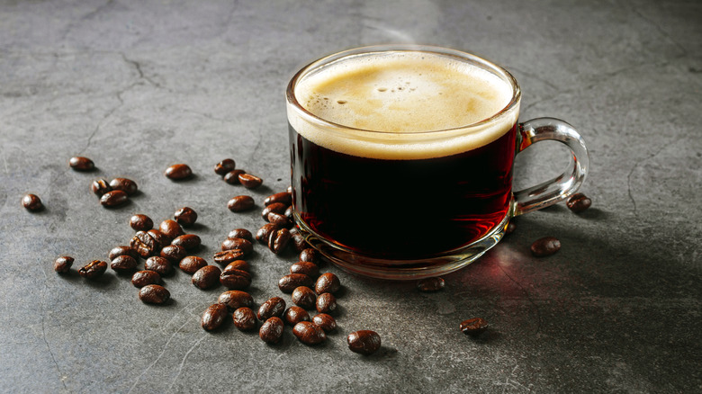 Mug of hot coffee beside whole roasted coffee beans