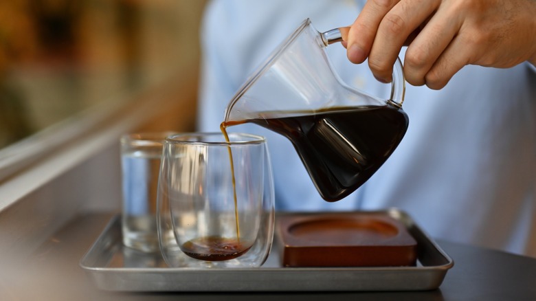 Hand pouring coffee from a glass pitcher to a cup