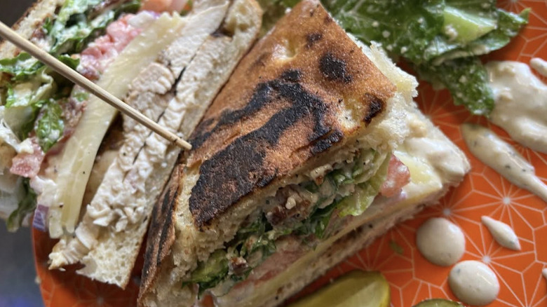 sandwich on a red plate filled with chicken, cheese and drop of dressing to the side