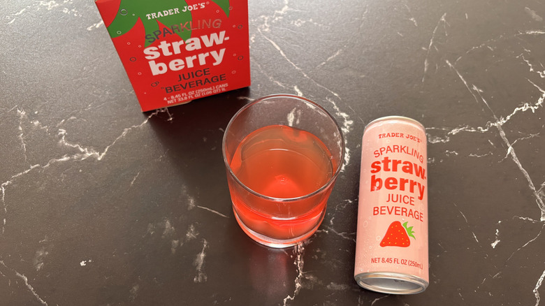 Trader Joe's sparkling strawberry juice beverage in glass next to can and product box