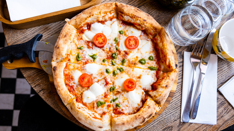 A Neapolitan style pizza on a wood table with silverware